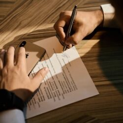 A person signing a lease agreement on a wooden desk with a smartphone placed nearby, symbolizing the process of securing a doctor office space for lease.